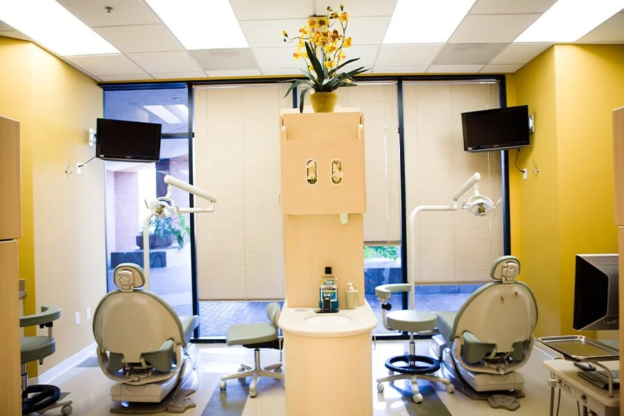 Dual dental operatory with yellow walls, chairs, and central cabinet.