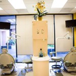 Dual dental operatory with yellow walls, chairs, and central cabinet.