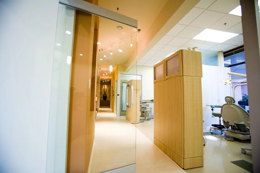 Clinic hallway with glass doors, wood cabinet, and visible treatment room.