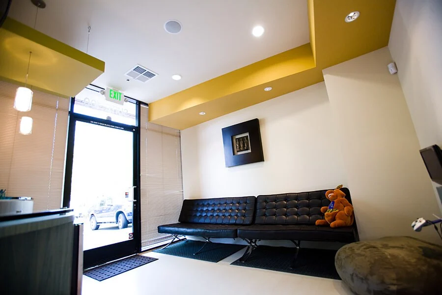 Waiting area with black leather bench, yellow ceiling accents, and teddy bear.