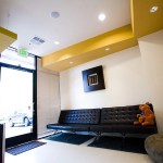 Waiting area with black leather bench, yellow ceiling accents, and teddy bear.