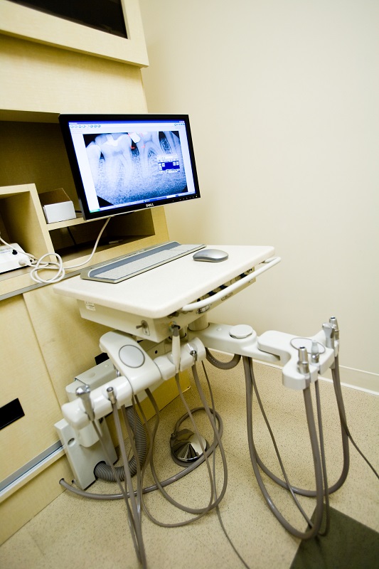 Dental X-ray monitor on adjustable desk with handpiece unit below.