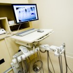 Dental X-ray monitor on adjustable desk with handpiece unit below.
