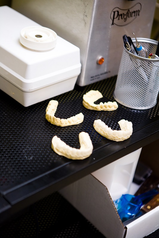 Four dental impression trays on a black countertop near lab equipment