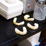 Four dental impression trays on a black countertop near lab equipment